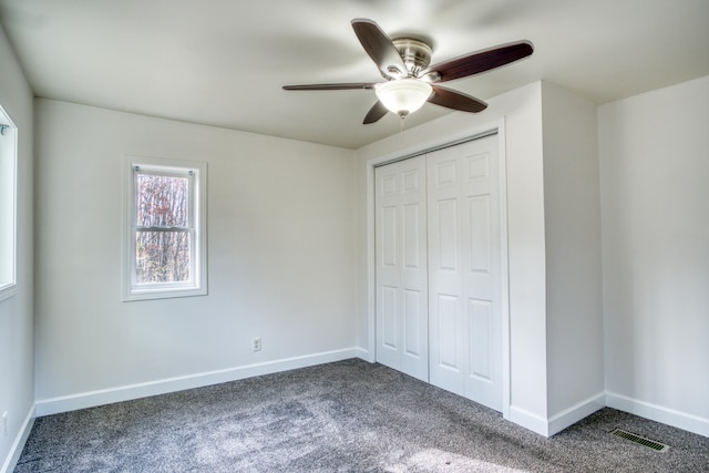 unfurnished bedroom with ceiling fan, dark carpet, and a closet