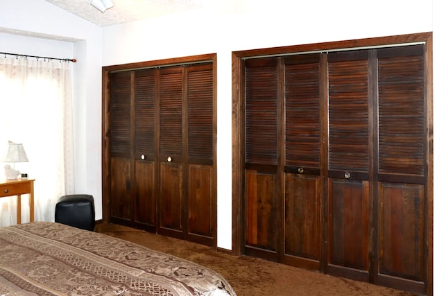 unfurnished bedroom featuring carpet, a textured ceiling, two closets, and lofted ceiling