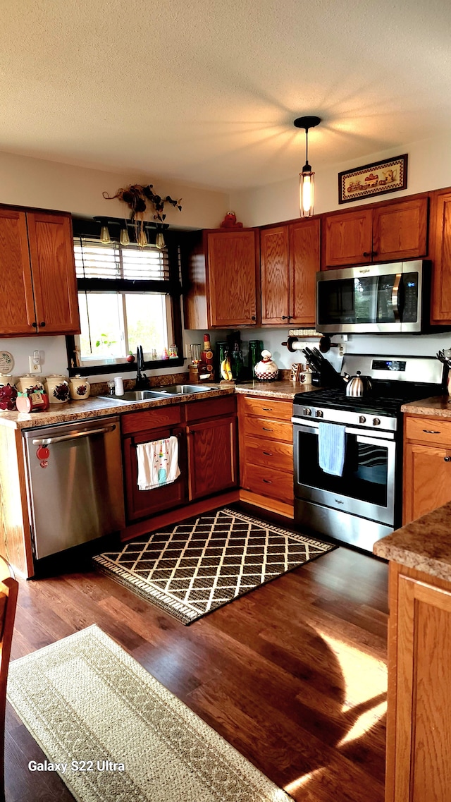 kitchen featuring hanging light fixtures, sink, light wood-type flooring, a textured ceiling, and appliances with stainless steel finishes