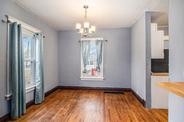 unfurnished dining area with dark wood-type flooring and a notable chandelier