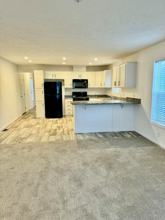 kitchen featuring kitchen peninsula, white cabinets, light hardwood / wood-style flooring, and black appliances