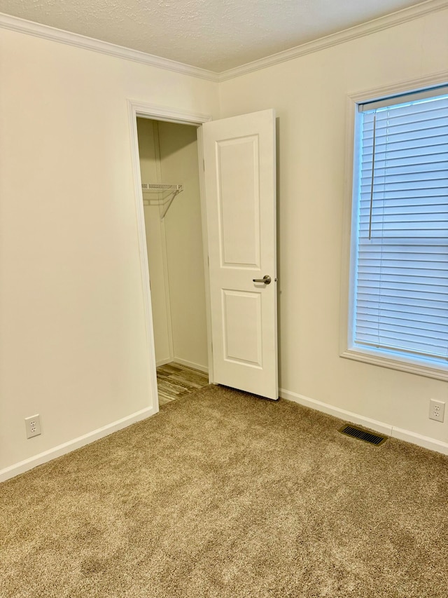 unfurnished bedroom with a textured ceiling, carpet floors, a closet, and crown molding