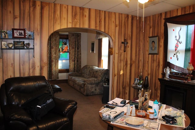 living room with carpet flooring, a fireplace, wooden walls, and a drop ceiling