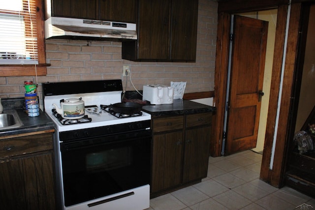 kitchen featuring white range with gas stovetop, light tile patterned floors, dark brown cabinetry, and decorative backsplash