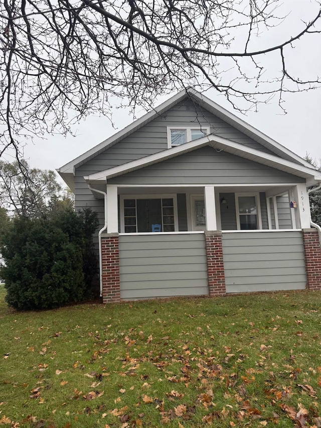 bungalow featuring brick siding, a porch, and a front lawn