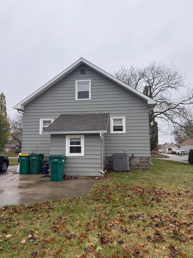 rear view of house featuring a patio, cooling unit, a yard, and a shingled roof