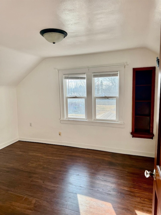 additional living space with dark wood-style floors, a textured ceiling, lofted ceiling, and baseboards