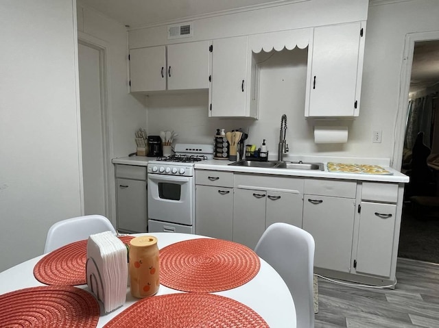 kitchen with white cabinets, light wood-type flooring, white range with gas cooktop, and sink