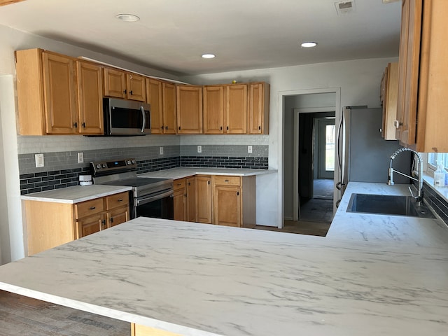 kitchen featuring kitchen peninsula, stainless steel appliances, tasteful backsplash, and sink