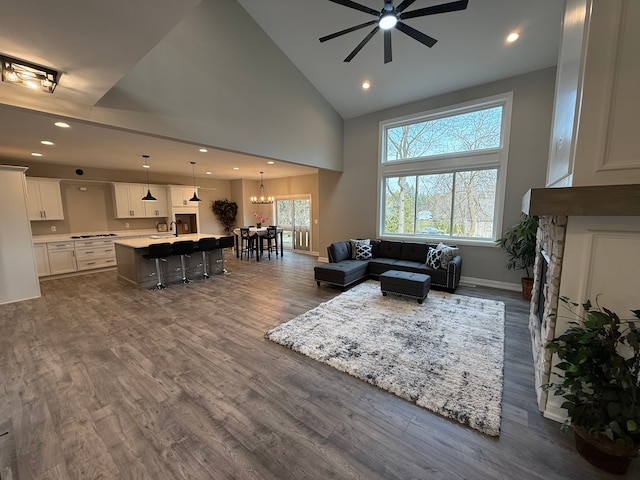 living room featuring ceiling fan with notable chandelier, a fireplace, high vaulted ceiling, and dark hardwood / wood-style floors