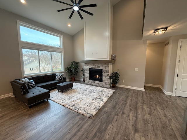 living room with dark hardwood / wood-style floors, ceiling fan, a towering ceiling, and a fireplace