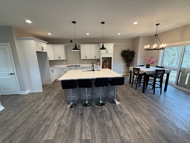 kitchen featuring hardwood / wood-style flooring, decorative light fixtures, white cabinetry, and an island with sink