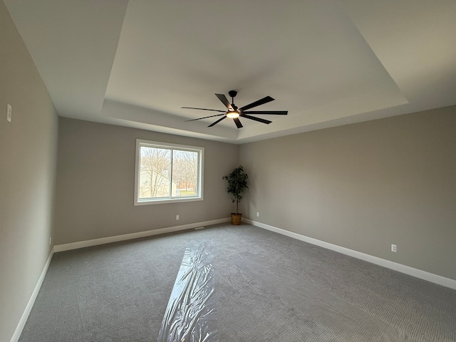 empty room with carpet, a raised ceiling, and ceiling fan