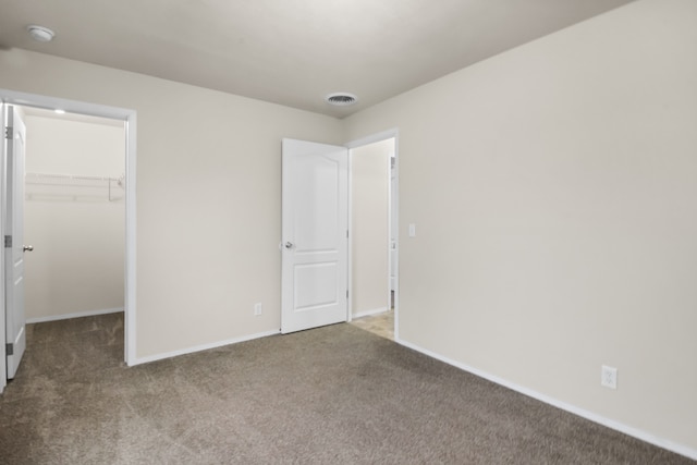 unfurnished bedroom with a walk in closet, a closet, and carpet floors