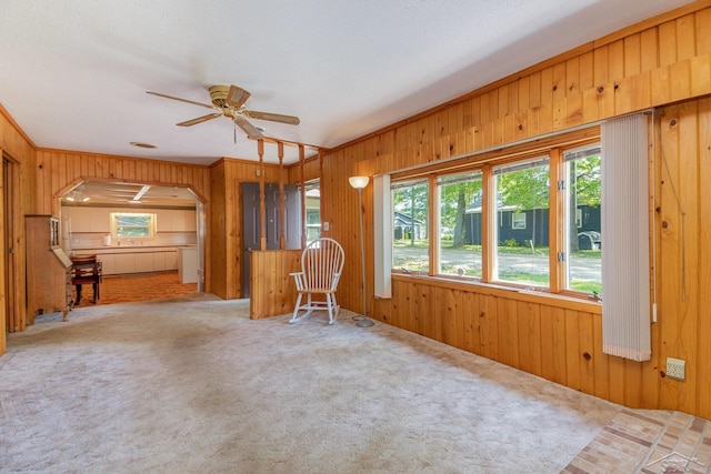 unfurnished living room with carpet flooring, ceiling fan, wood walls, a textured ceiling, and ornamental molding