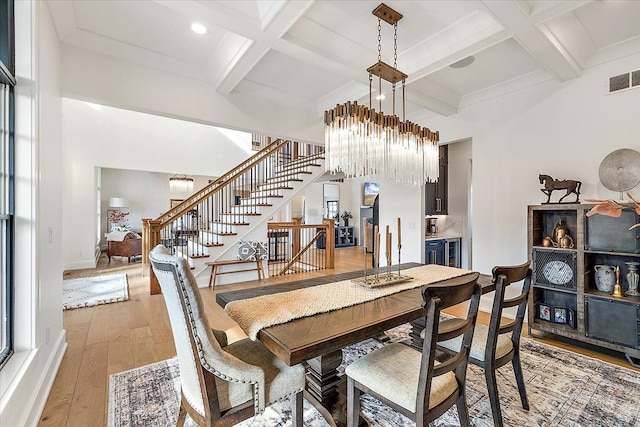 dining space featuring light hardwood / wood-style flooring, beamed ceiling, a chandelier, and coffered ceiling