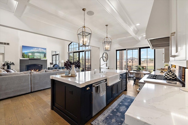 kitchen with dishwasher, sink, light hardwood / wood-style floors, pendant lighting, and a kitchen island with sink