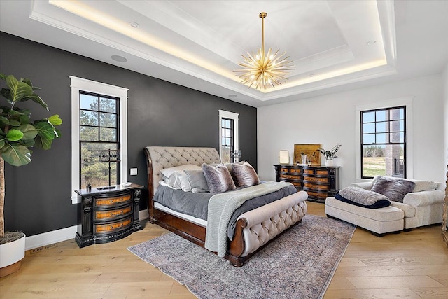 bedroom with light wood-type flooring, a raised ceiling, multiple windows, and a notable chandelier