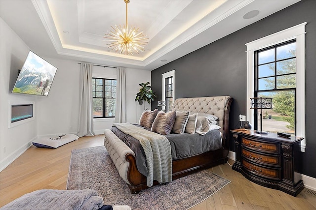 bedroom featuring a chandelier, light wood-type flooring, a raised ceiling, and multiple windows