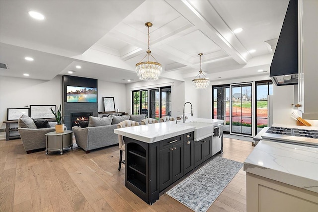 kitchen with light stone countertops, sink, decorative light fixtures, a fireplace, and a center island with sink