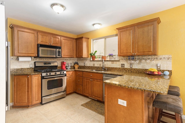 kitchen featuring a breakfast bar, stone counters, sink, appliances with stainless steel finishes, and kitchen peninsula