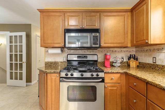 kitchen featuring decorative backsplash, light stone countertops, light tile patterned floors, and stainless steel appliances