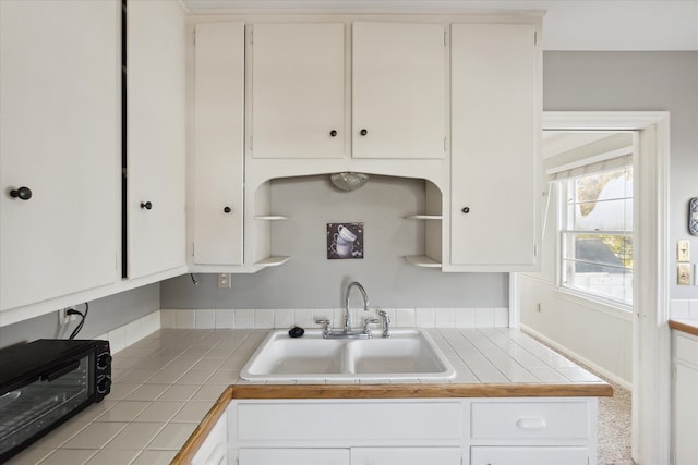 kitchen with tile countertops, white cabinetry, and sink