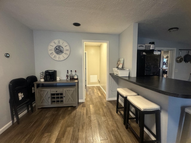 interior space featuring dark wood-type flooring, a breakfast bar area, kitchen peninsula, and a textured ceiling