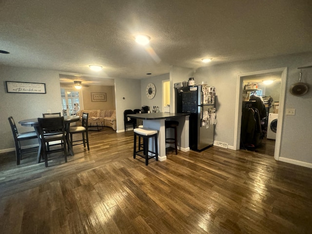 kitchen featuring stainless steel refrigerator, washer / dryer, a breakfast bar area, ceiling fan, and dark wood-type flooring