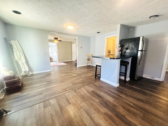 kitchen featuring a breakfast bar area, stainless steel fridge, dark hardwood / wood-style floors, a textured ceiling, and kitchen peninsula