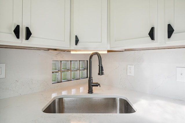 room details featuring backsplash, light stone countertops, sink, and white cabinets