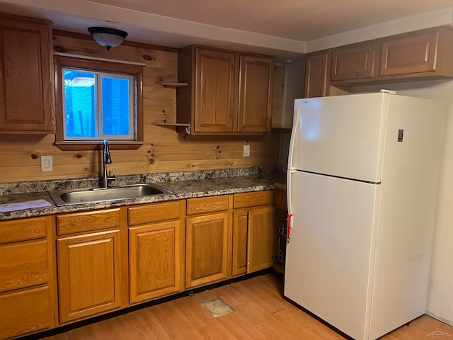 kitchen with white fridge, sink, wooden walls, and light hardwood / wood-style flooring