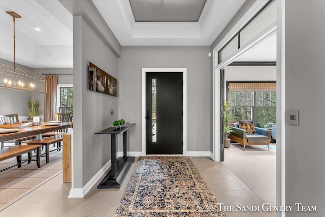 entrance foyer with a raised ceiling, crown molding, and a notable chandelier