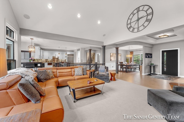 living room with lofted ceiling, light hardwood / wood-style floors, ornate columns, and an inviting chandelier