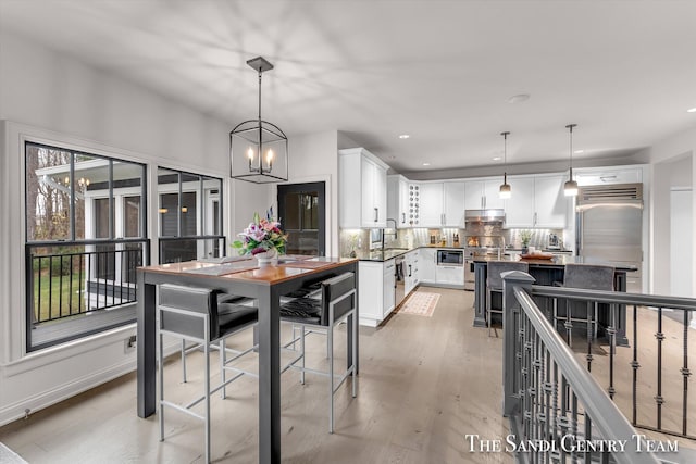 kitchen with white cabinetry, tasteful backsplash, a notable chandelier, decorative light fixtures, and light wood-type flooring