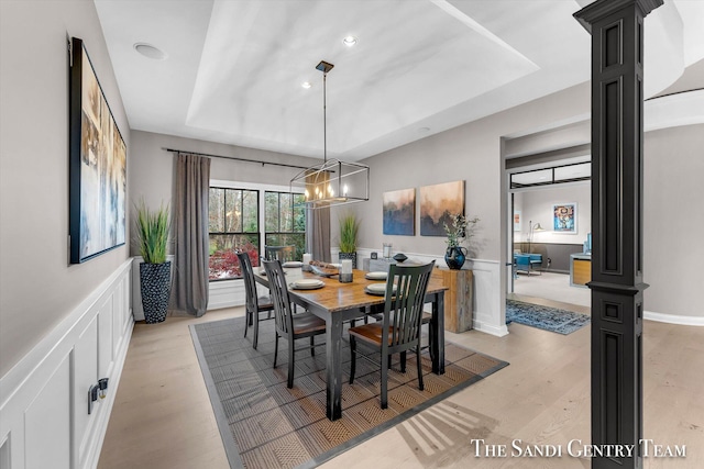 dining space with light hardwood / wood-style floors, an inviting chandelier, ornate columns, and a tray ceiling