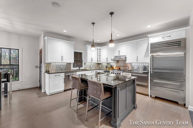 kitchen featuring appliances with stainless steel finishes, tasteful backsplash, light hardwood / wood-style flooring, dark stone countertops, and white cabinets