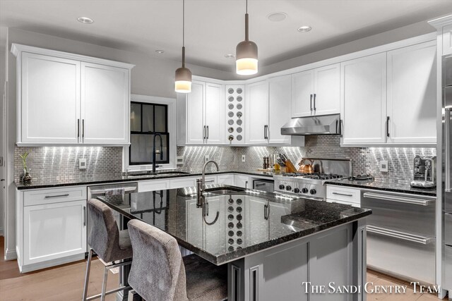 kitchen featuring pendant lighting, a center island with sink, sink, dark stone countertops, and stainless steel range oven