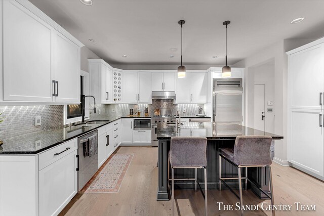 kitchen with a center island with sink, sink, built in appliances, light hardwood / wood-style floors, and white cabinetry