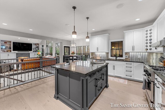 kitchen featuring white cabinets, light hardwood / wood-style flooring, high end stainless steel range oven, and an island with sink