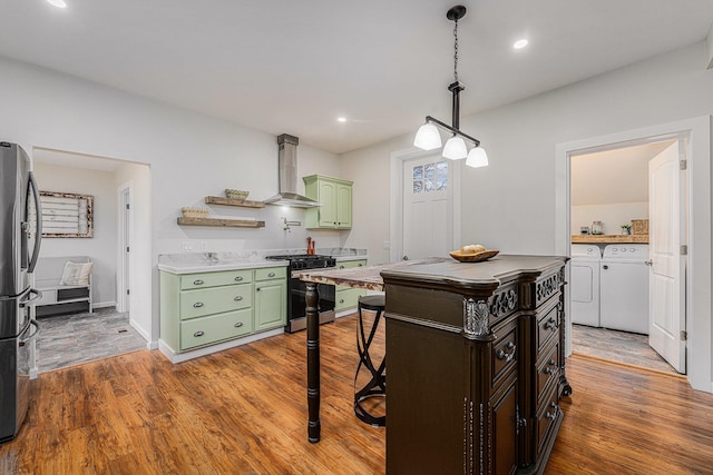 kitchen with appliances with stainless steel finishes, hardwood / wood-style floors, separate washer and dryer, green cabinetry, and wall chimney range hood