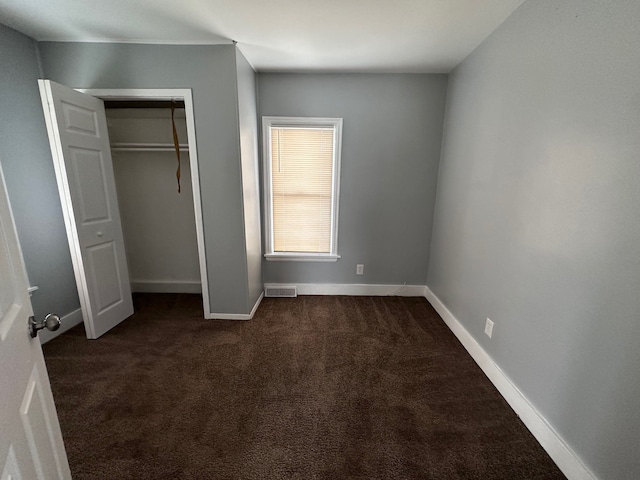 unfurnished bedroom featuring dark carpet and a closet