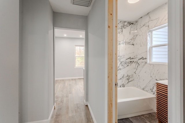 bathroom featuring wood-type flooring, a bathtub, and tile walls