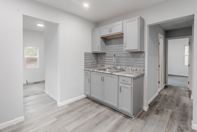 kitchen with backsplash, light stone counters, light hardwood / wood-style flooring, and sink