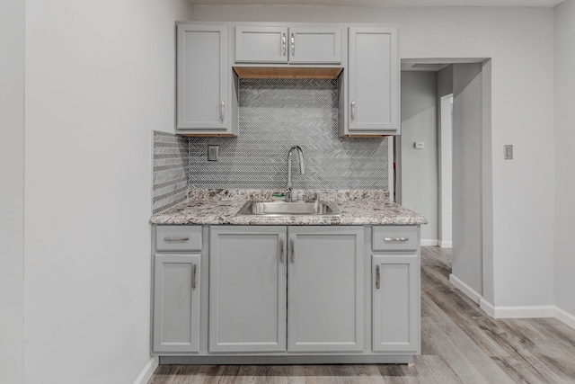 kitchen featuring decorative backsplash, light stone countertops, sink, and light hardwood / wood-style flooring