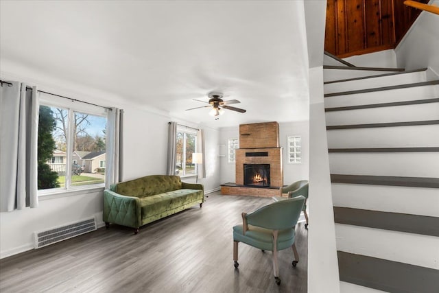 living room featuring ceiling fan, a stone fireplace, and wood-type flooring