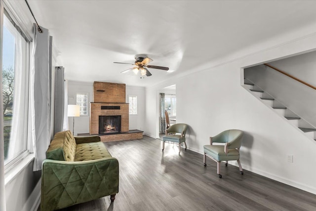 living room featuring a large fireplace, ceiling fan, a healthy amount of sunlight, and dark wood-type flooring