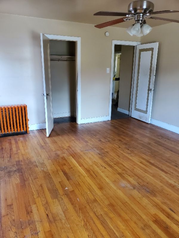 17366 Monica St, Detroit, MI 48221 - unfurnished bedroom featuring radiator, light wood-style flooring, baseboards, a closet, and ceiling fan