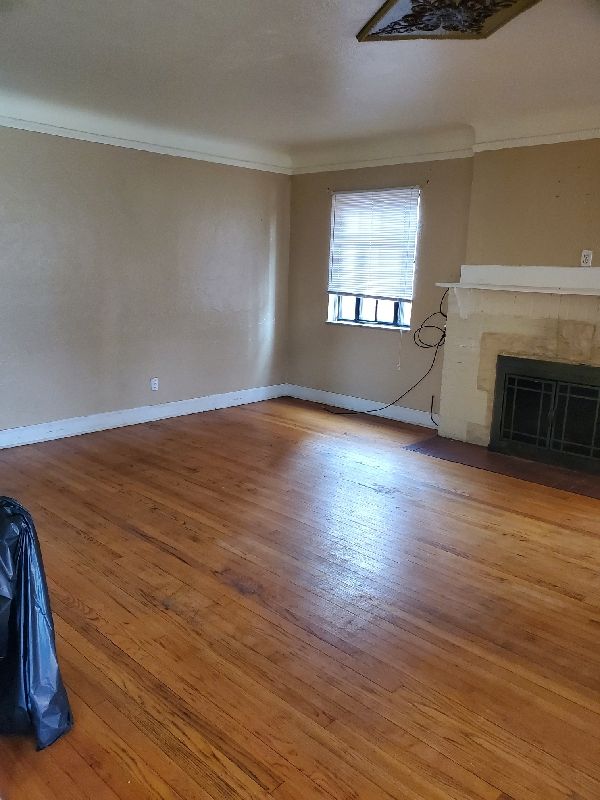 17366 Monica St, Detroit, MI 48221 - unfurnished living room featuring crown molding, a fireplace, wood finished floors, and baseboards