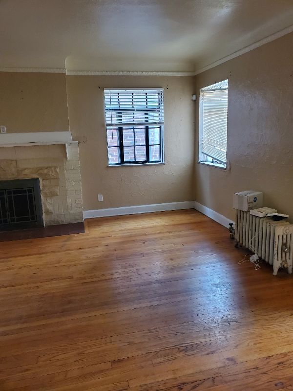 17366 Monica St, Detroit, MI 48221 - unfurnished living room featuring crown molding, wood finished floors, baseboards, a fireplace, and radiator